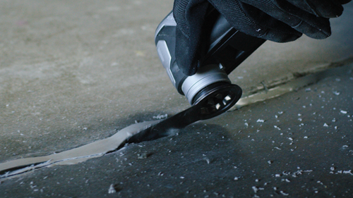 A gloved hand using a power tool to cut a line in a surface.