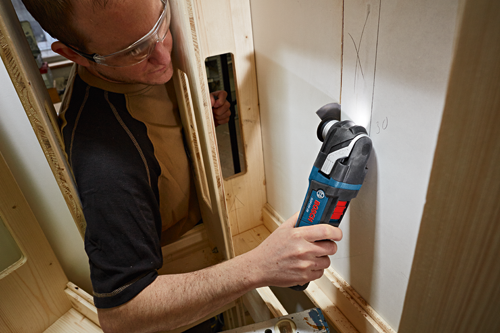 Person wearing safety glasses using a Bosch GOP18V-28 to cut a drywall panel.