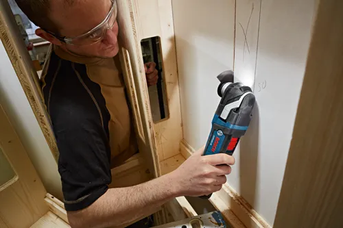 Person wearing safety glasses using a Bosch GOP18V-28 to cut a drywall panel.