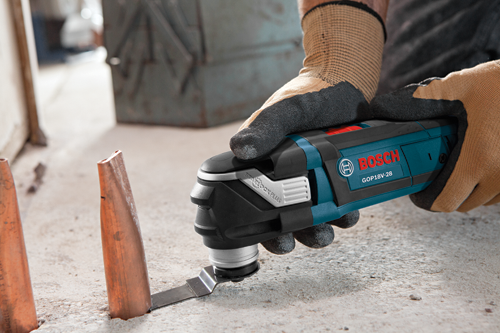 Bosch GOP18V-28 multi-tool being used to cut into a concrete surface, with copper tubing nearby.