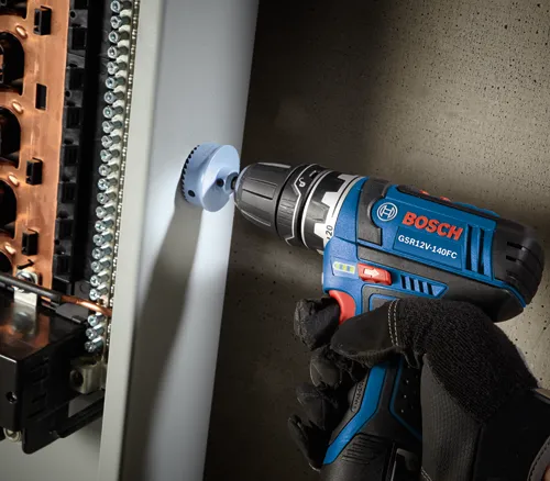 Bosch GSR12V-140FC drill with 1-1/2" hole saw cutting a hole in an electrical panel.