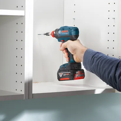 Bosch Lithium-Ion cordless drill screwing into a white cabinet shelf, with 18V 4.0Ah battery.