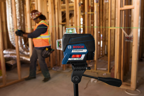 Bosch Professional GLL3-330CG Green Laser level on a tripod, with a person wearing a hard hat and safety vest in the background.