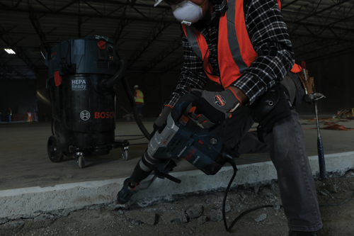 Man using Bosch 11264EVS Boschhammer with a HEPA Ready vacuum cleaner nearby.