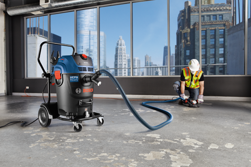 Bosch GA4201A HEPA Ready vacuum, connected to a worker using a grinder in a construction site, with a cityscape in the background.