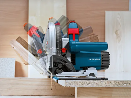 Bosch GKT13-255 saw cutting wood, with visible measurements in mm and degree markings.
