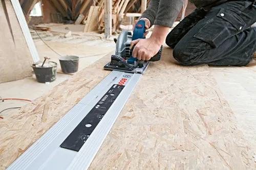 Person using a Bosch FSN 2100 Professional guide rail system with a circular saw on a wood surface.