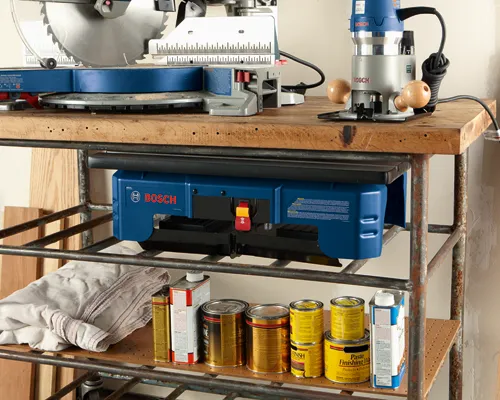 Bosch RA1141 miter saw and router on a workbench, with additional Bosch tool and various cans of finish products on a lower shelf.