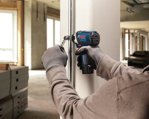 Person using a Bosch Lithium-Ion 12V impact wrench to tighten a bolt on a pipe. The wrench is held with gloves.