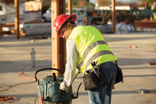 Construction worker wearing a red hard hat and yellow safety vest, inspecting a vacuum cleaner.