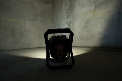 A portable work light shines in a dark, concrete-walled space.