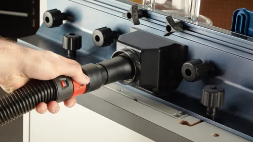 Hand connecting a black and red hose to a dark-colored machine.