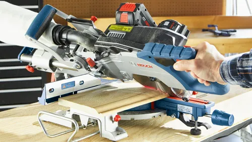Bosch miter saw cutting wood, with a person holding the blue and gray handle.