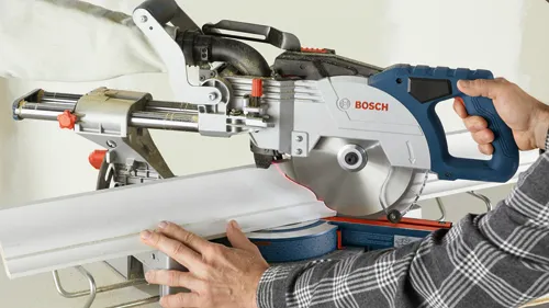 Bosch miter saw cutting a white wooden board, with a person wearing a checkered shirt handling the tool.