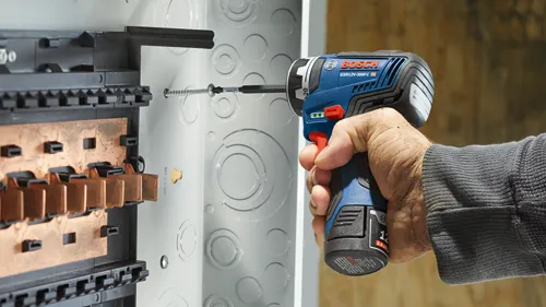 Bosch GSR12V-300FC HD cordless drill being used to drive a screw into an electrical panel; hand visible.