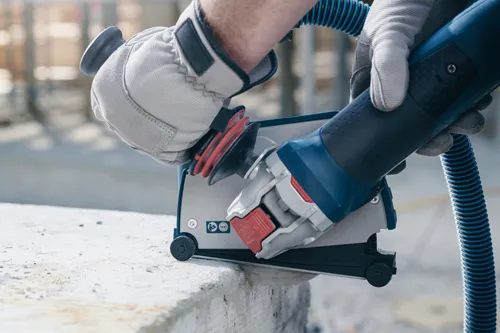 Bosch electric concrete saw, with red and silver accents, held by gloved hands, cutting concrete.