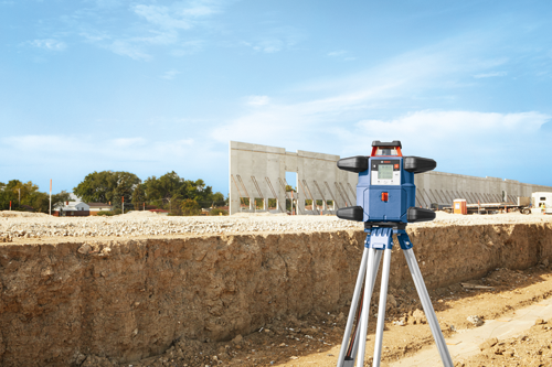 Bosch construction laser level on a tripod, at a construction site.