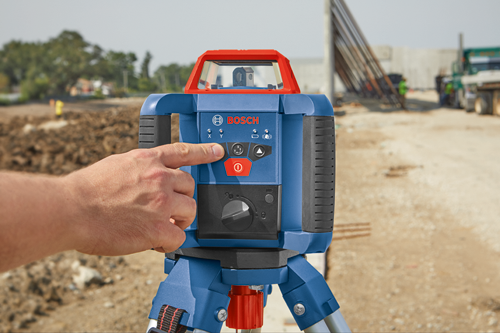 Bosch laser level, a hand presses a red button on its control panel.