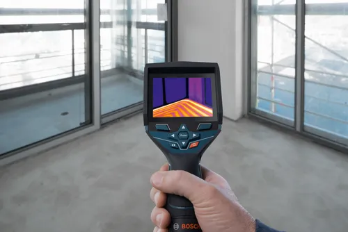 Bosch thermal imaging camera held by a person, displaying a thermal image of a room. "Func" and power buttons are visible.