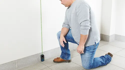 Man kneeling next to a wall, holding a device with a green line extending to the top, reading “9” and “BLADE”.