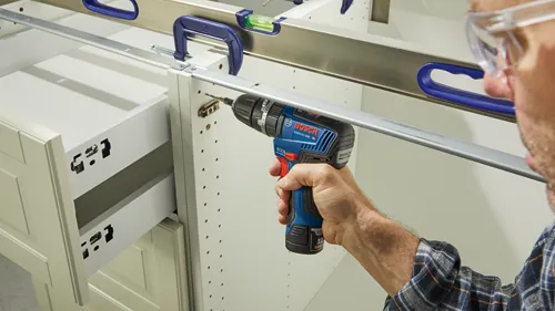 Bosch GSB12V-300 HD cordless drill being used to install cabinetry hardware.