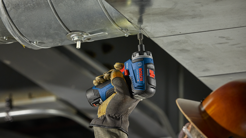 Bosch GSR12V-300HX cordless drill is drilling a screw into an air duct, held by a gloved hand. A hard hat is visible in the background.