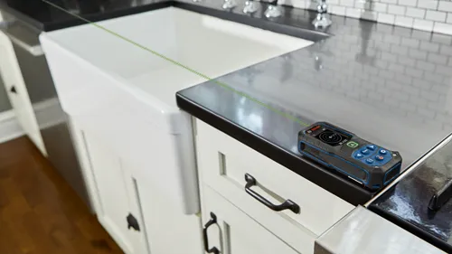 Bosch BLAZE laser measure projecting a green beam onto a countertop with visible text "BOSCH".