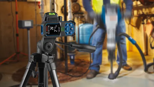 Bosch BLAZE laser distance meter with display showing "26' 2" 15/16" attached to tripod, with a person operating a jackhammer in the background.