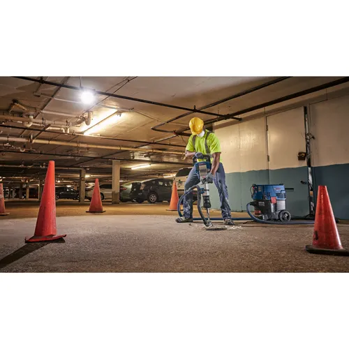 Person wearing a yellow hard hat and work clothes operates a Bosch demolition hammer. A Bosch HEPA Ready vacuum cleaner is nearby.