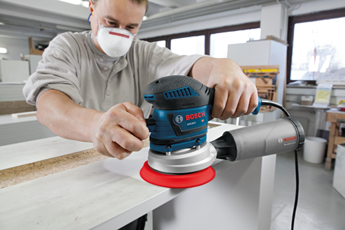 Person wearing a face mask using a Bosch GEX34-6 random orbit sander.