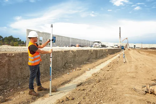 Person wearing orange safety vest using survey equipment on a construction site.