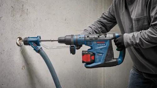 Bosch GBH18V-40C HD BITURBO BRUSHLESS hammer drill with dust collection attachment being used to drill into a concrete wall. A person is holding the drill.
