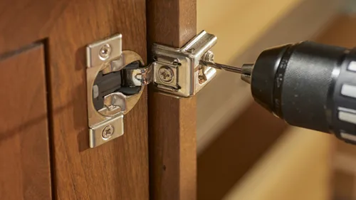 Drill bit installing a hinge on wooden cabinet door.