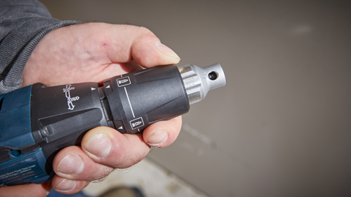 Hand holding a Bosch power drill with a directional arrow.