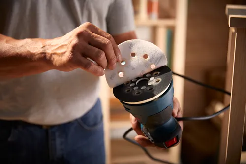 Person holding Bosch sander, inserting sanding paper with "P80" printed on it.