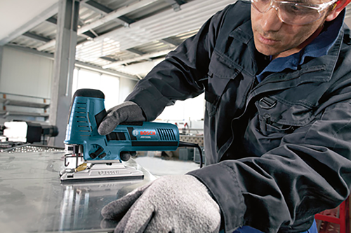A person wearing safety glasses and gloves using a Bosch jigsaw.