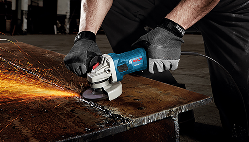 Man in work gloces using a Bosch corded angle grinder on metal with sparks flying.