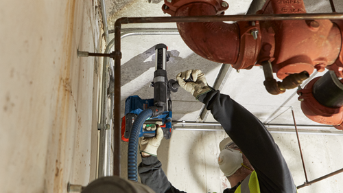 Man wearing safety glasses and gloves using a Bosch hammer drill.