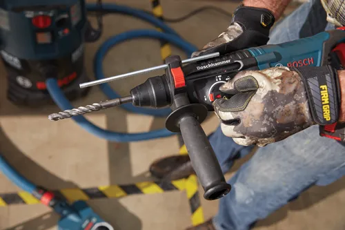 Boschhammer electric drill with attached drill bit, held by a person wearing camo gloves with the word "BOSCH" visible.