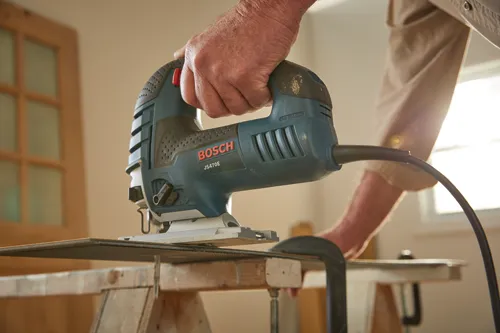 Man using the Bosch corded JS470E corded jig saw to cut laminate flooring.