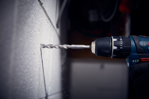 Bosch drill drilling a hole in a wall. Drill bit is visible, and the drill has an adjustable speed setting.