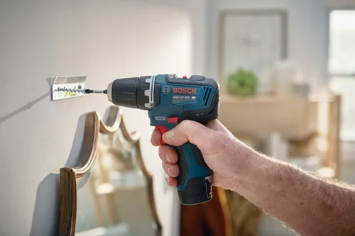 Bosch GSR12V-300 HD drill driving screw into wall, held by person.