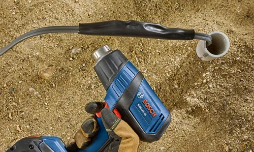 Bosch GHG18V-50 heat gun pointed at a black cable that is connected to a white tube.