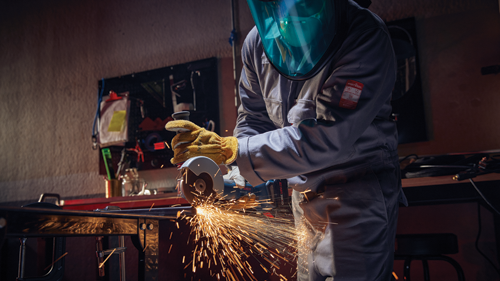 Person wearing protective gear uses a grinder, sparks flying.