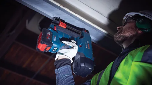Man wearing hard hat and safety glasses using a Bosch GNB18V-12 Turbo Brushless nail gun.