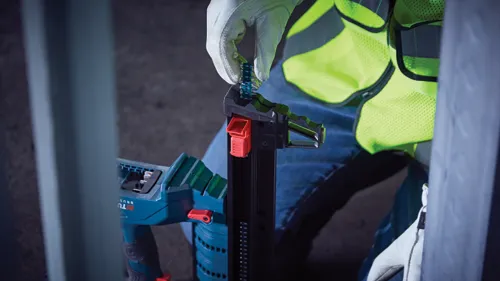 Person wearing a safety vest and gloves is holding a nail gun, inserting nails.