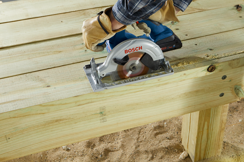 Bosch cordless circular saw cutting a wood plank, with visible text "BOSCH" and "18V".