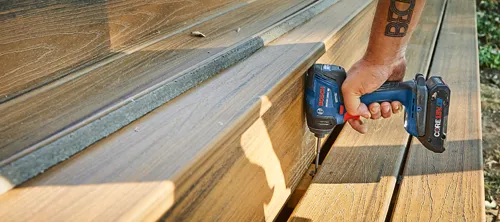 Bosch GDR18V-1800C impact driver with CORE18V 4.0 Ah battery being used to drive a screw into a wood surface; tattoo on forearm is visible.