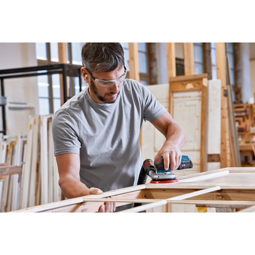 A person wearing safety glasses and earplugs uses a Bosch sander on a wooden frame.