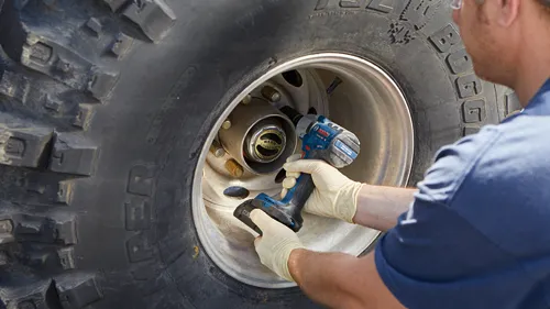 Bosch GOS18V-330C BRUSHLESS MOTOR power tool on a wheel, a person wearing a blue shirt and gloves is working on the wheel.